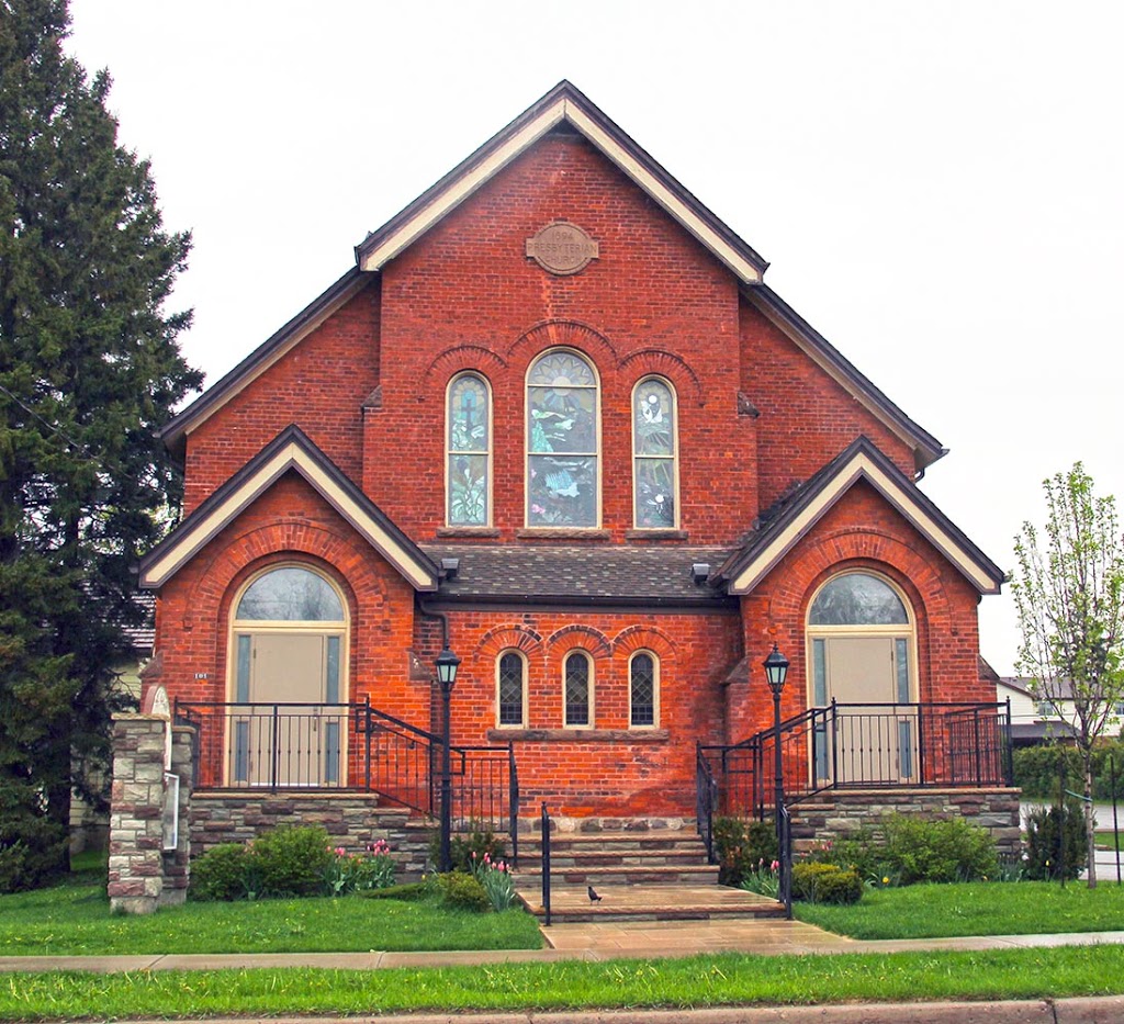 A red brick church with two entrance doors and three stained glass windows.